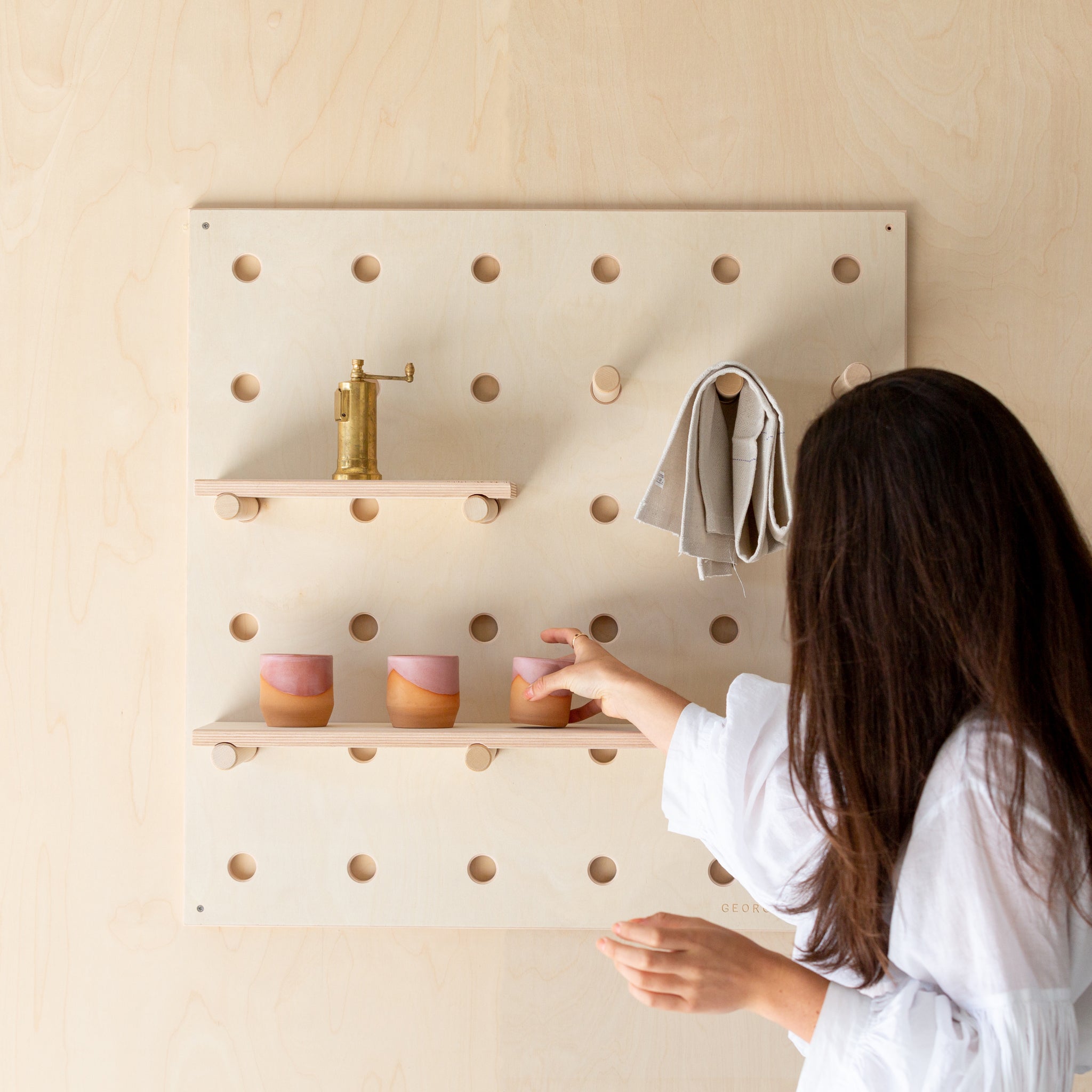 A wooden pegboard with dowel pegs and shelves designed for storing belongings or displaying products in a store